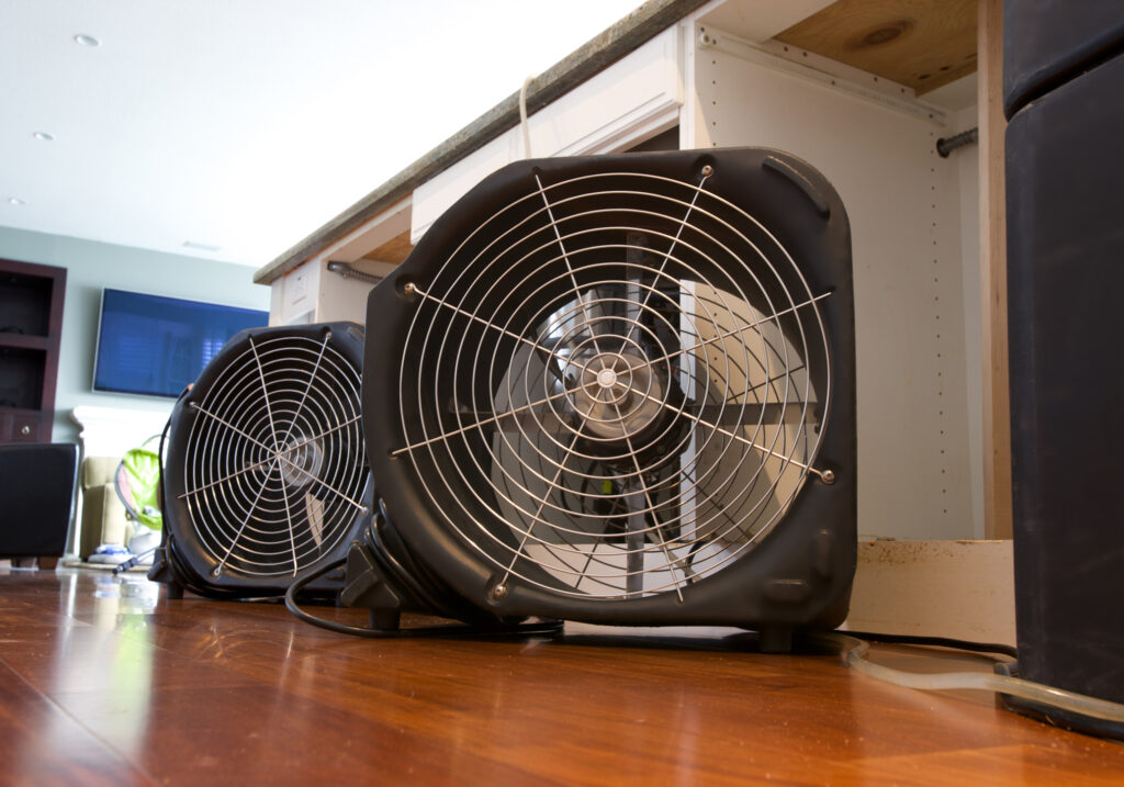 Two industrial fans running to dry out water damaged residential kitchen