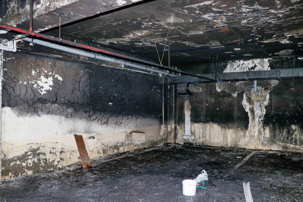 A basement with soot and water damage from a fire with the walls and ceiling are blackened and stained